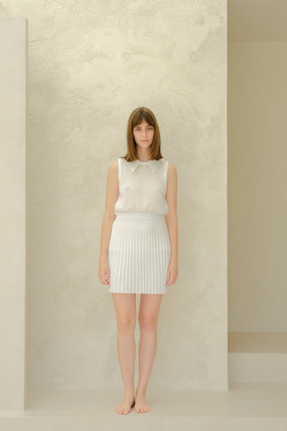 Figura intera of a modella con a bianco mesh sleeveless top con a collarosso neckline e a bianco plissé minigonna, barefoot.