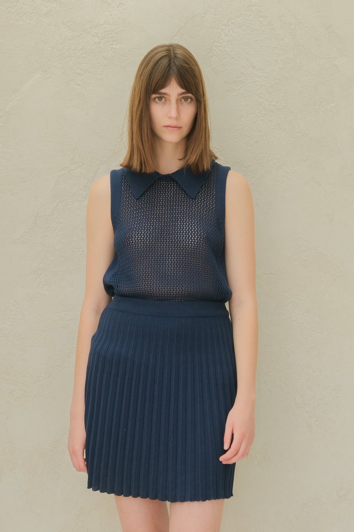Blu navy top in maglia senza maniche con a mesh pattern e a colletto a punta, abbinata a a blu navy pleated minigonna.