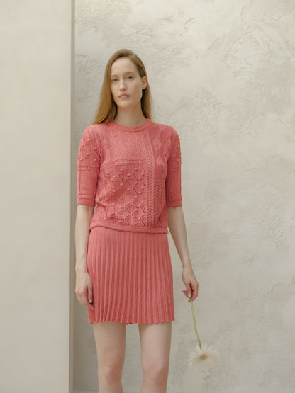Vista frontale of a model in a rosa minigonna plissé in cotone fine e top in maglia coordinato davanti a una parete chiara testurizzata.