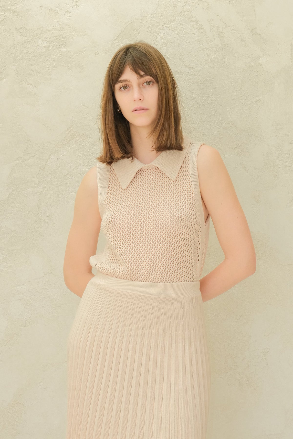 Modella con crema top in maglia senza maniche con a colletto a punta e a matching pleated minigonna.