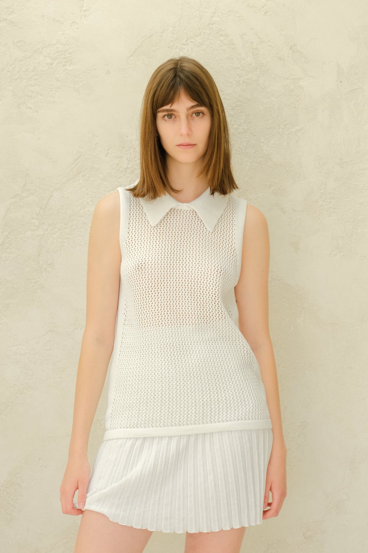 Modella con a bianco mesh sleeveless top con a collarosso neckline e a bianco plissé minigonna.