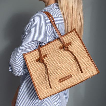 Rectangular straw effect shoulder bag with tan leather trim and handles worn over the shoulder.