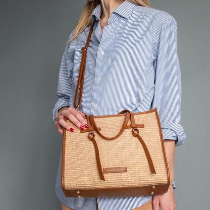 Close-up of rectangular straw effect bag with brown leather trim and top handles.