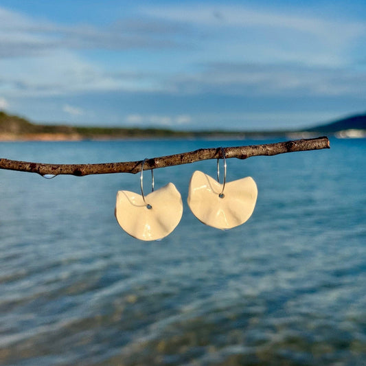 Frolla white ceramic dangle earrings hanging from a branch over a blue sea