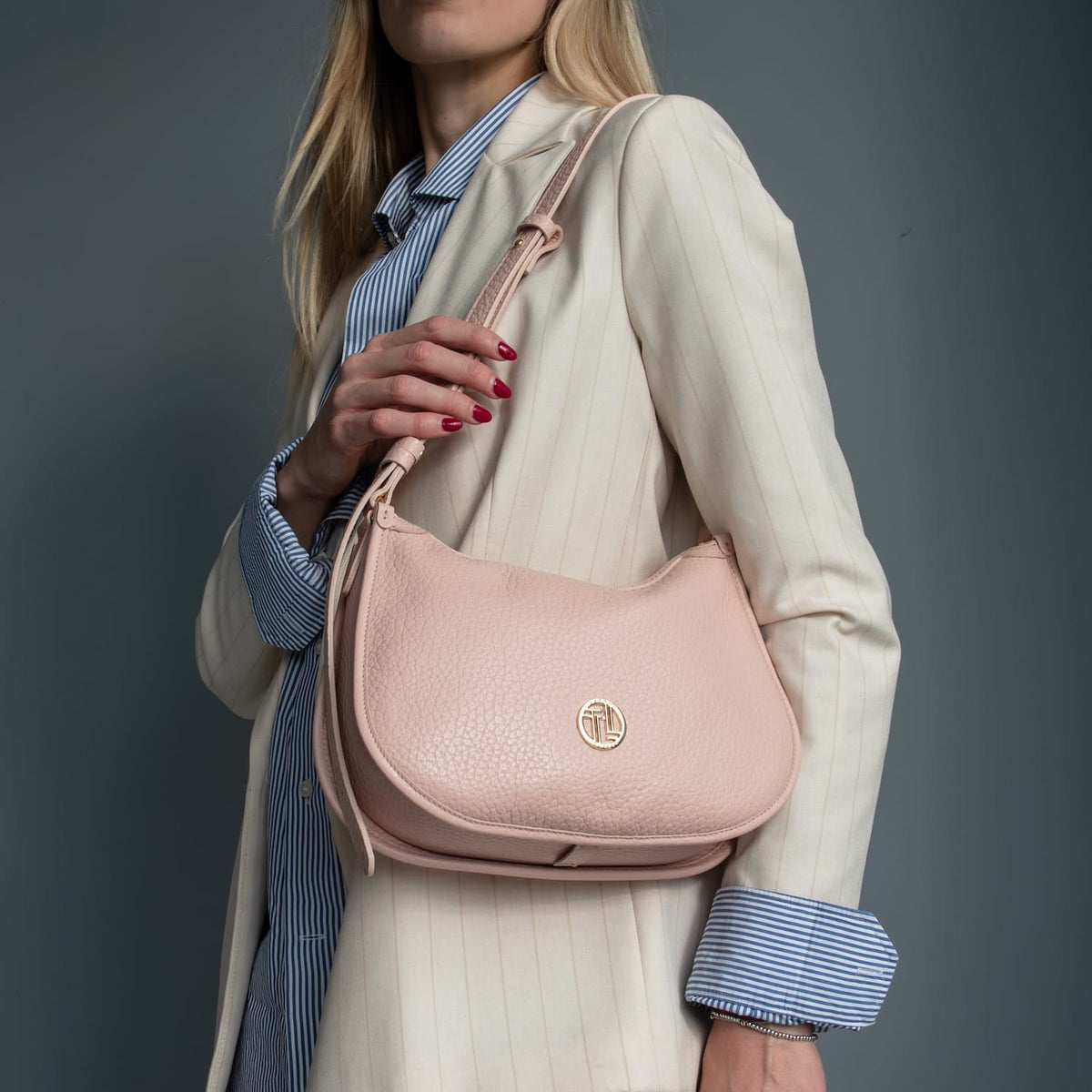 Rosa suave piel granulada Hoblò hobo bag with a logo dorado carried over the shoulder by a model in a cream pinstripe blazer