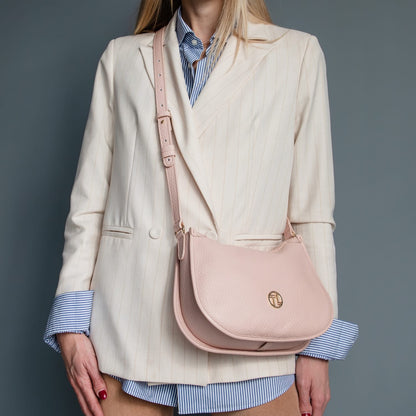 Blush pink Hoblò piel suave hobo bag with an correa ajustable worn crossbody against a cream blazer and blue striped shirt