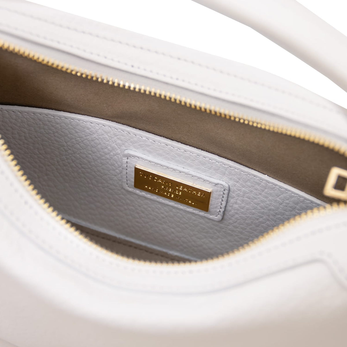 Vista interior of white Hoblò piel suave hobo bag showing light grey lining and a gold plate plaque.