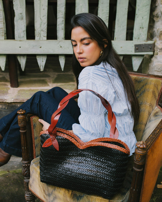 Léafa - Handwoven Leather Shoulder Bag | Brown & Black showcasing a woven black leather body with brown leather handles resting on a chair.