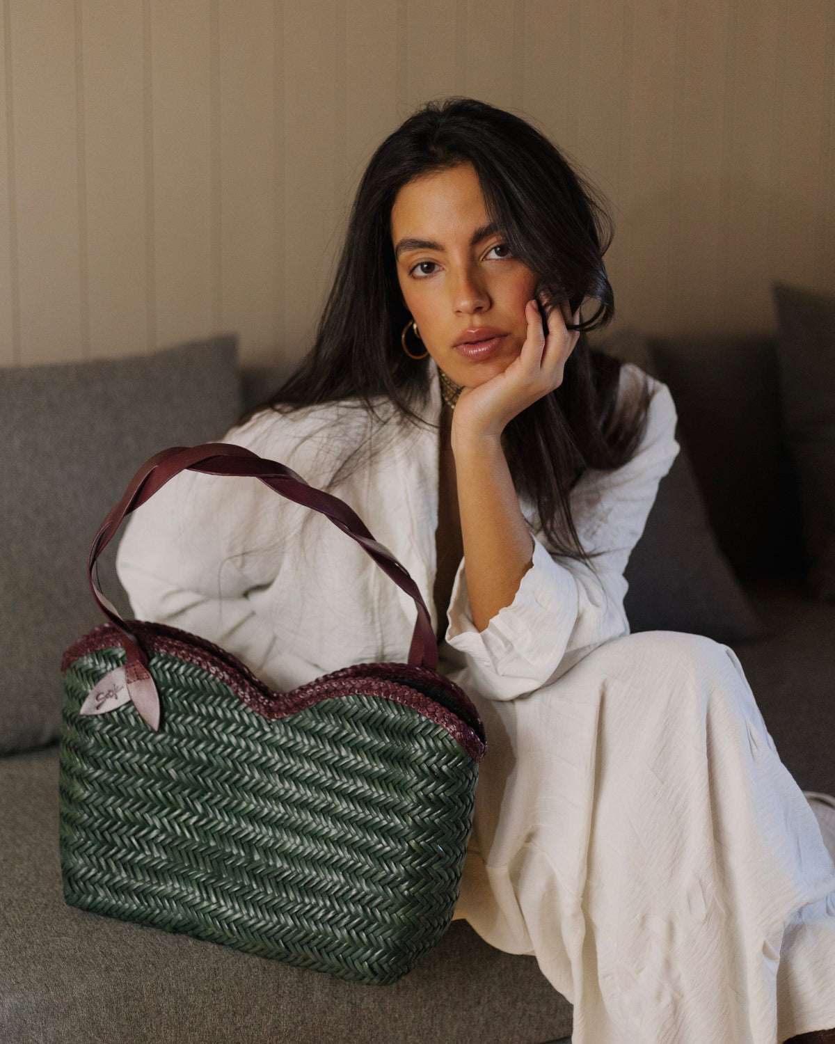 Léafa - Hewoven Leather Shoulder Bag | Bordeaux & Verde showing a woven verde leather body con bordeaux leather heles e trim placed on a couch.