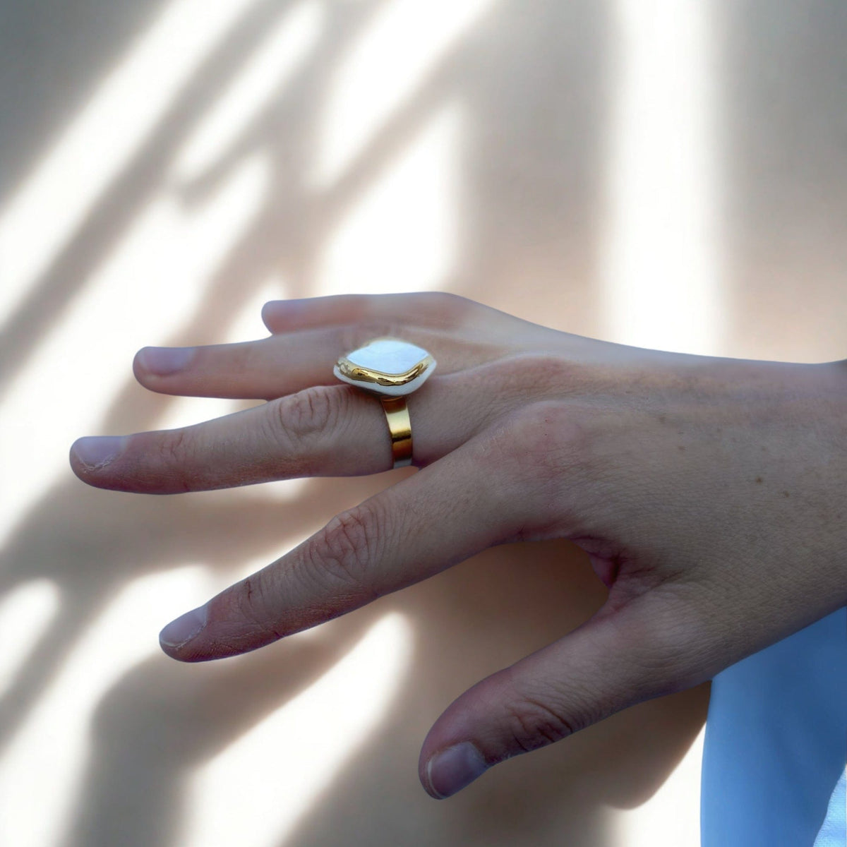 Vue latérale of a gold ring with a white ceramic top on a finger