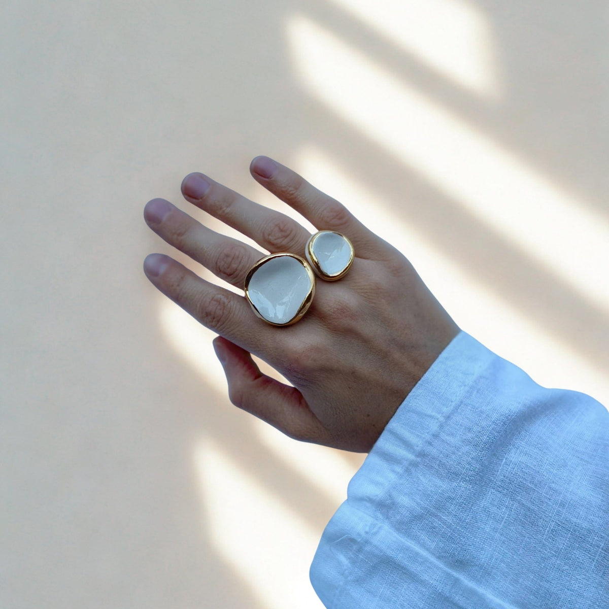 Hand wearing two handcrafted white ceramic rings with gold rims on the middle and ring fingers