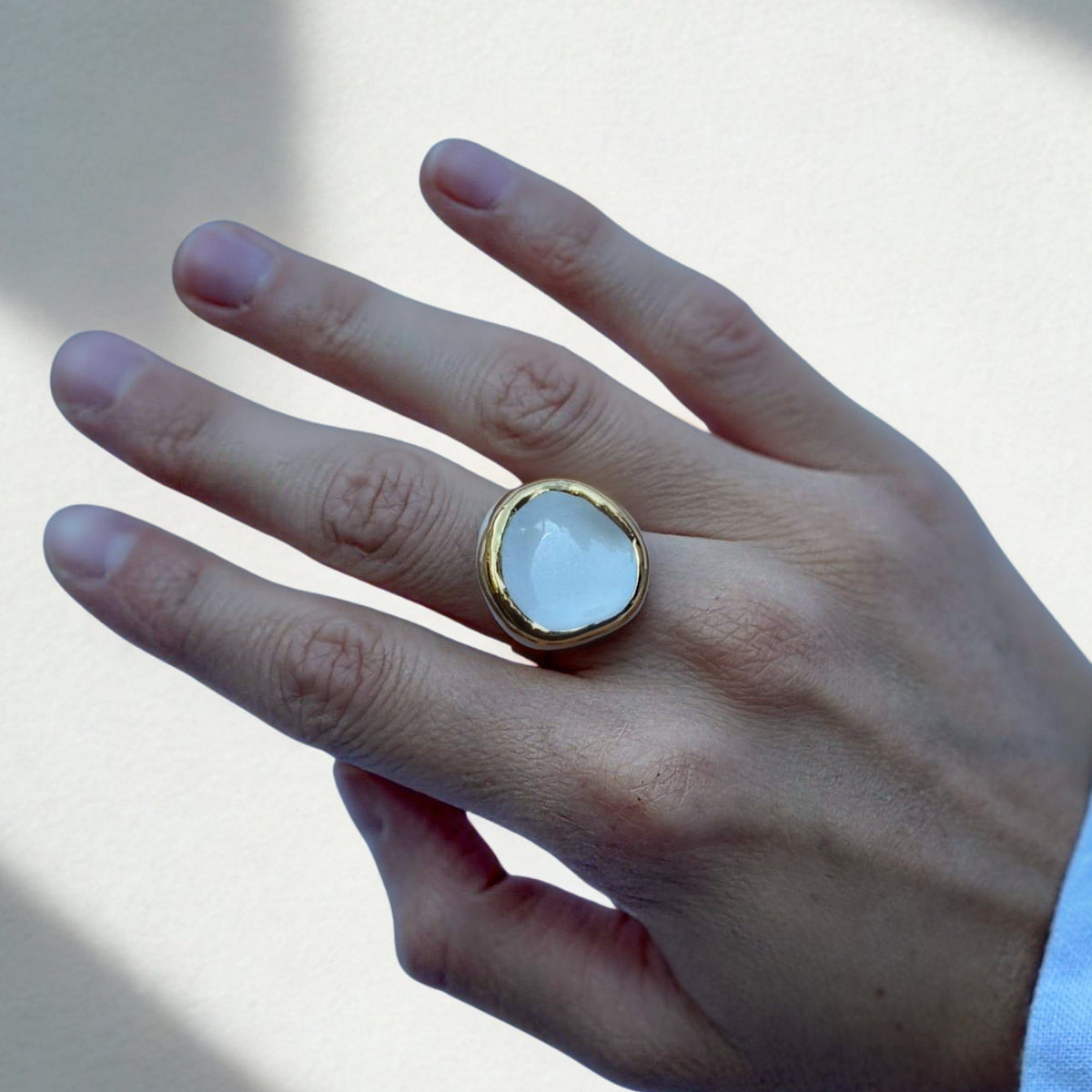 Gros plan of a gold band ring featuring a white ceramic top on a finger