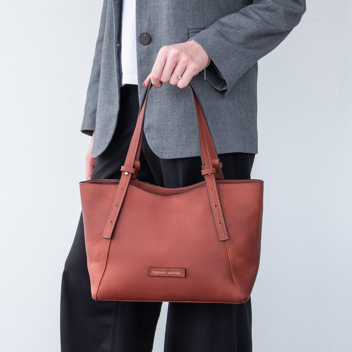 Libra long handle brown leather tote bag held in hand against a gray blazer