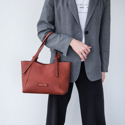 Person holding a brown leather Libra handbag against a plain background