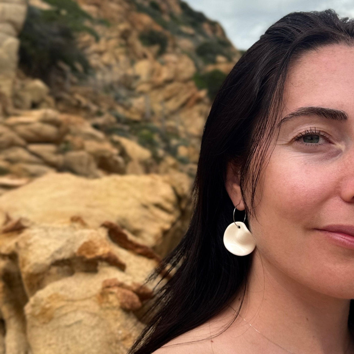 Close-up of a woman wearing handcrafted white ceramic dangle earrings with irregular discs
