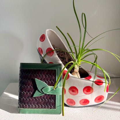 Lumi - Handwoven Leather Wallet | Vert&Dark Café with woven dark coffee leather and green leather trim beside a white pot with red dots and plant.