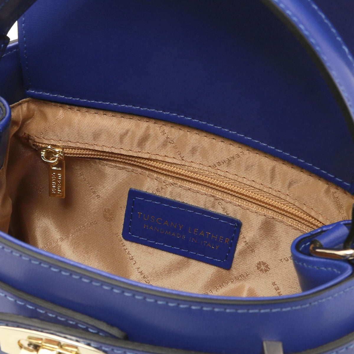 Interior of blue Maisy leather top handle bag showing beige lining, zip pocket and brand patch