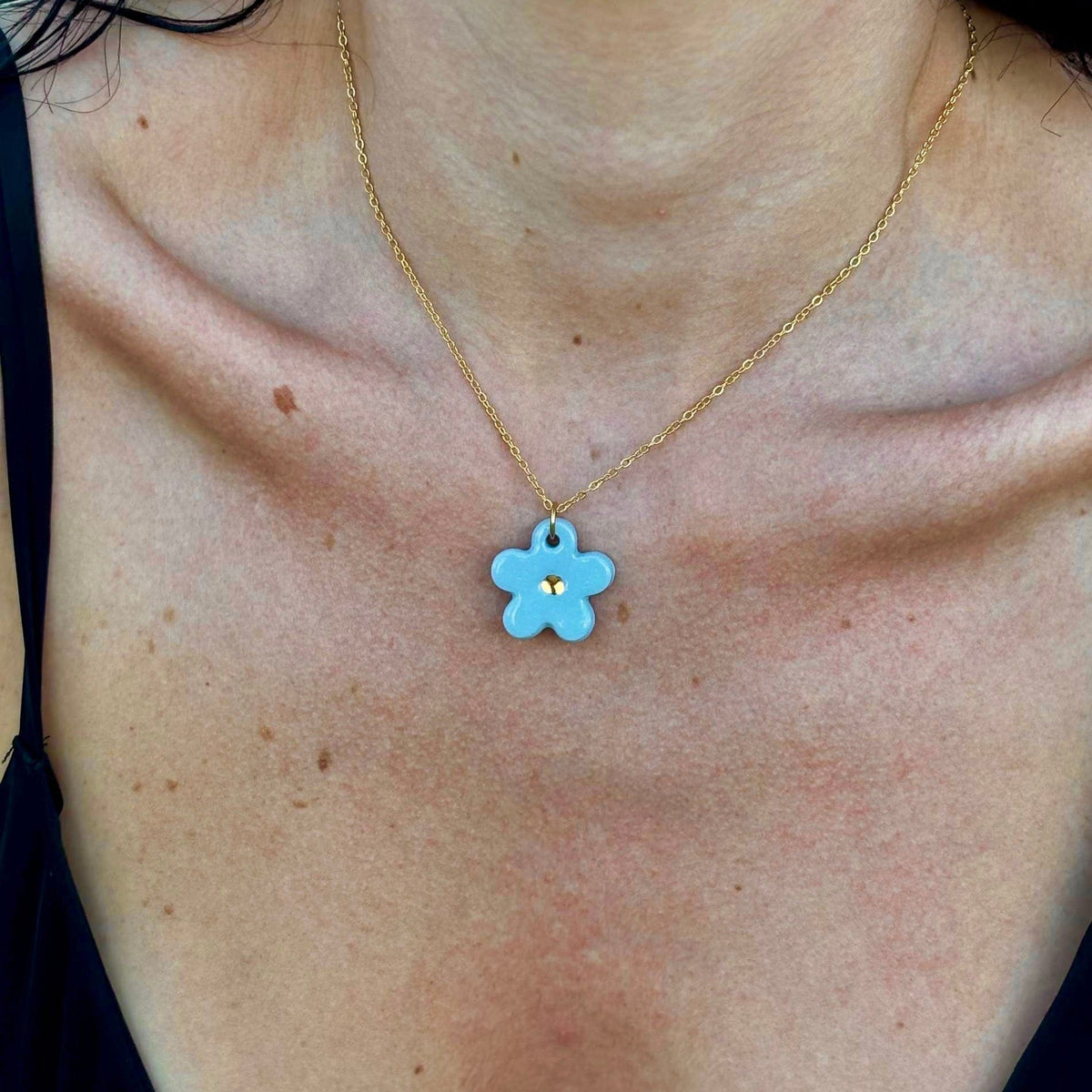 Azzurro flower ceramic pendant con a gold center on a gold chain
