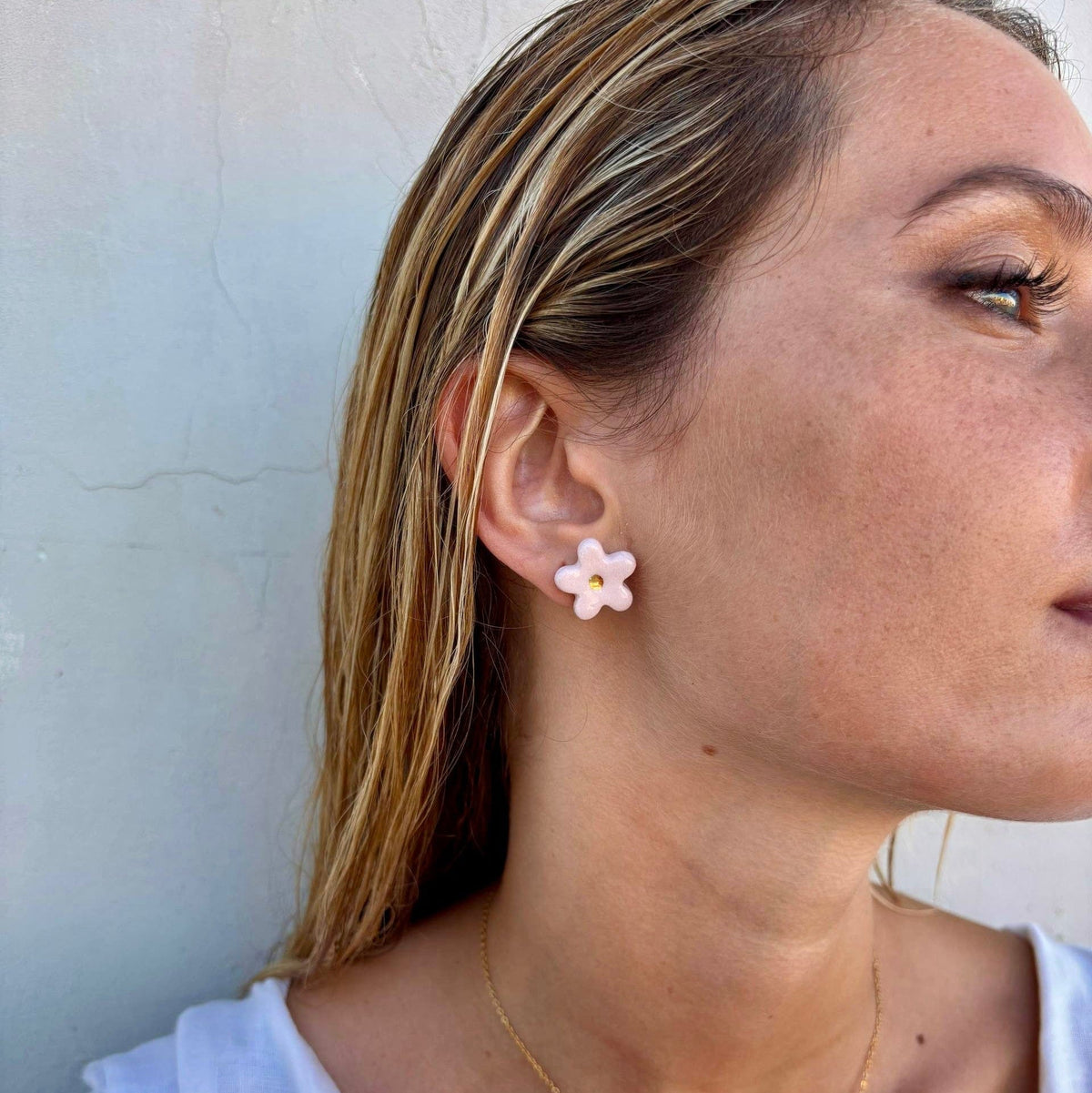 Zijaanzicht of a pink floral ceramic stud earring with gold center on the model's ear