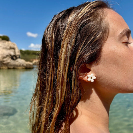 Woman with wet hair wearing white Margherita ceramic earrings by a clear body of water with rocky formations.