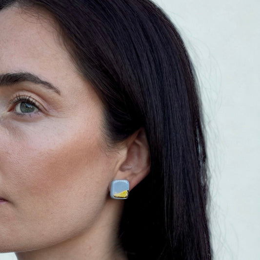 Side view of a model wearing a square light blue ceramic earring with a gold accent.