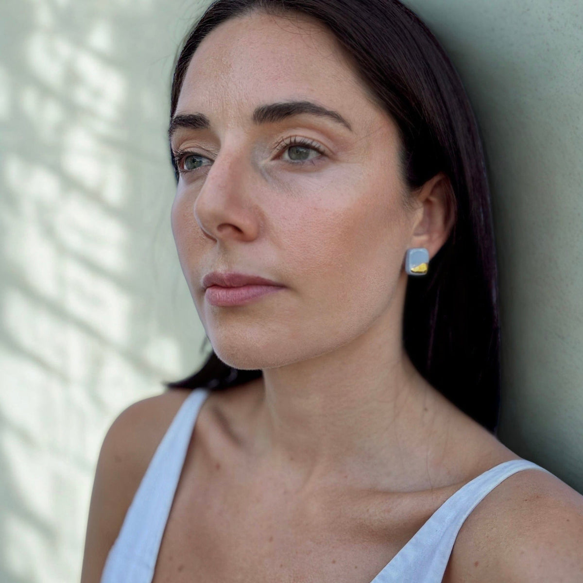 Close-up of a model wearing a square light blue ceramic earring with gold detail in profile.