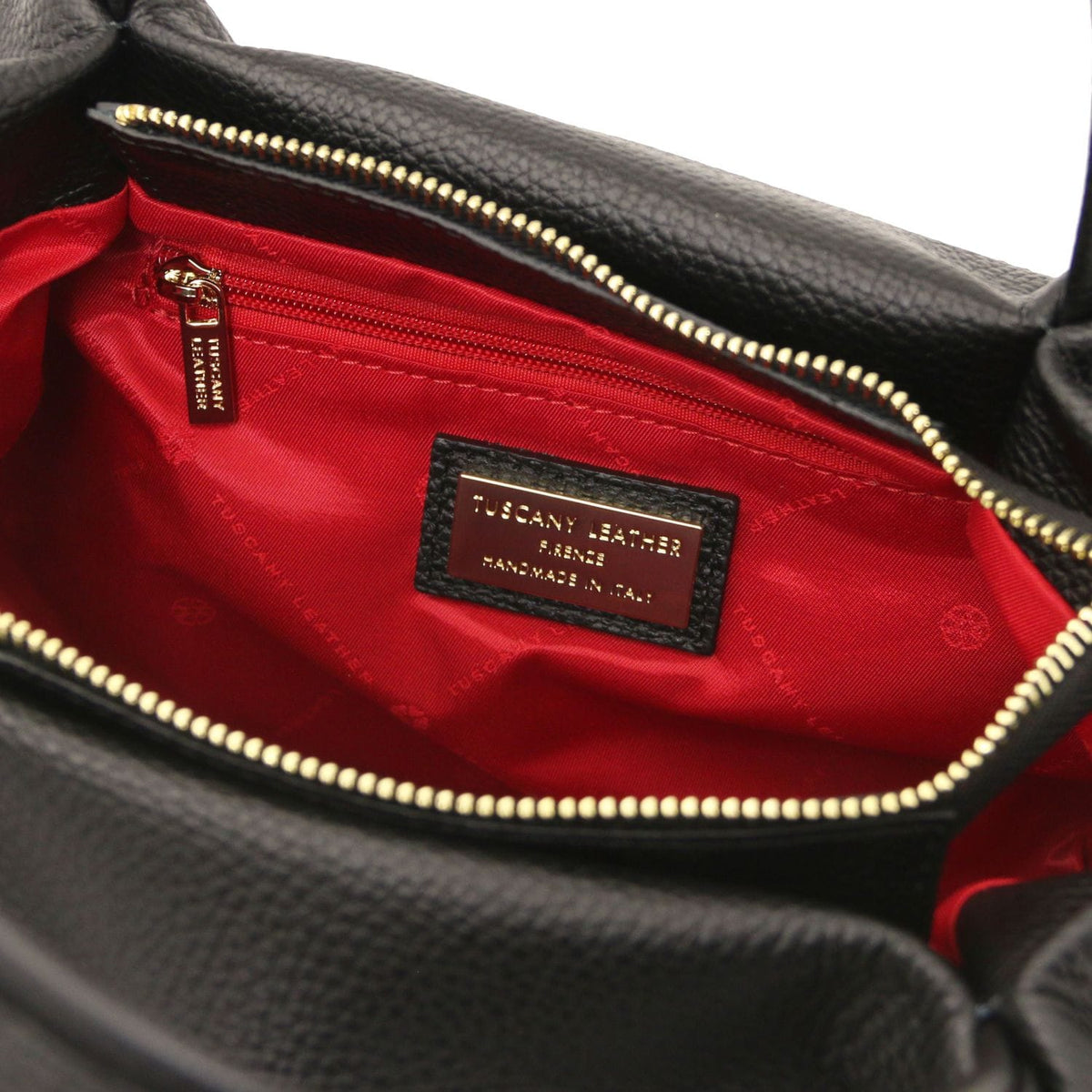 Open top of black Nora soft leather bag showing red lining, gold zipper, and brand label inside.