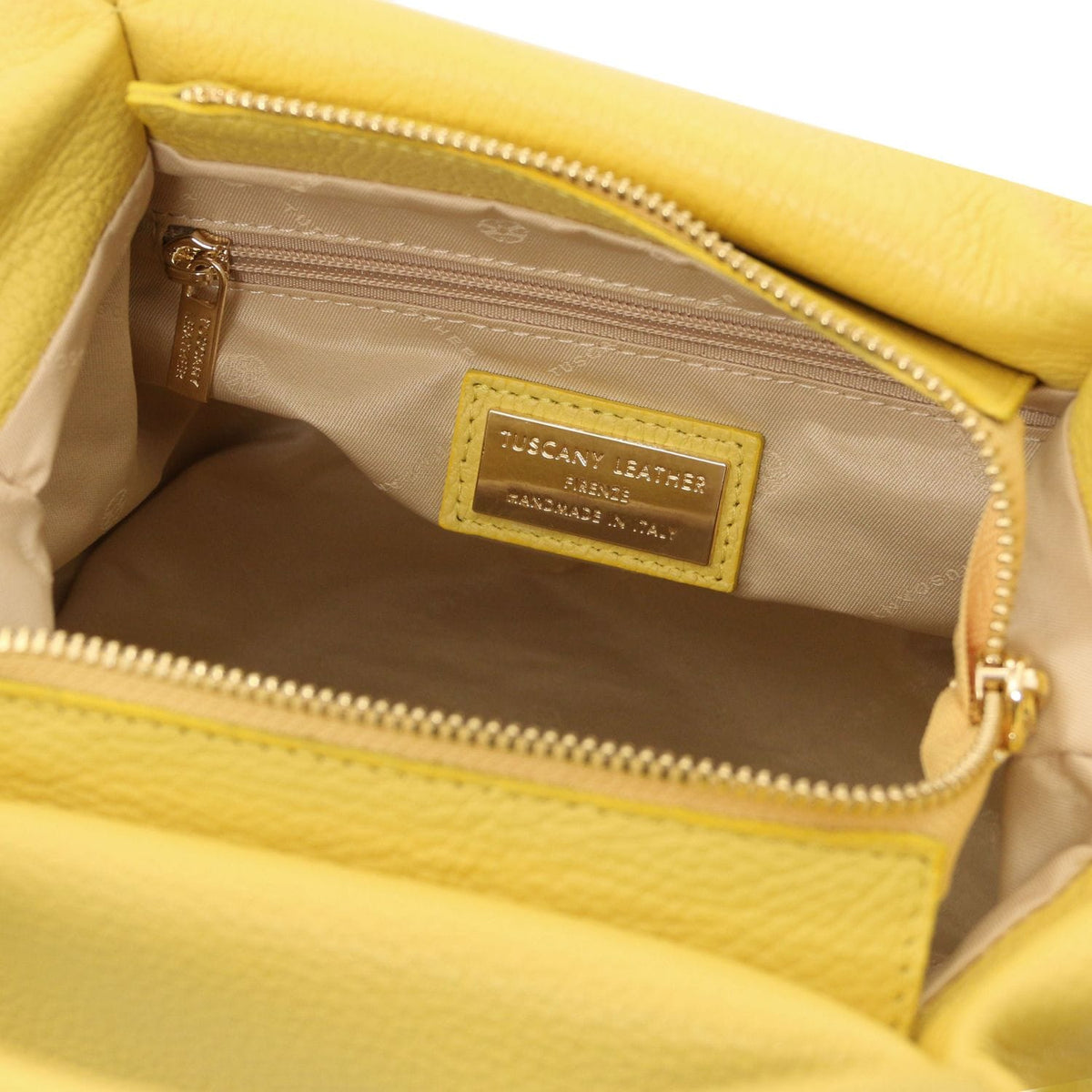 Open view of soft yellow leather handbag interior with zip pocket and beige fabric lining showing brand label.