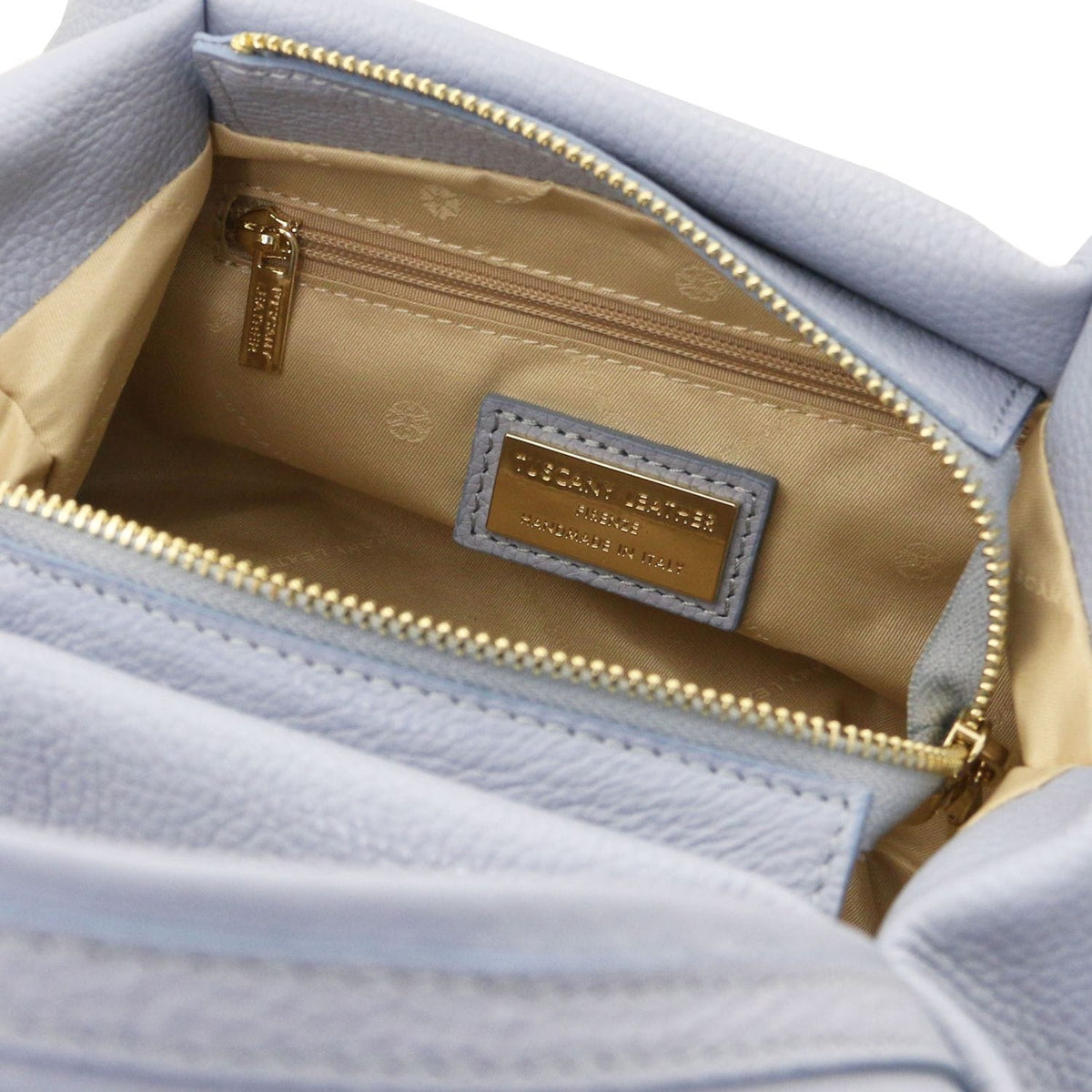 Open light blue Nora soft leather handbag interior with beige lining a gold zip pocket and a gold brand plaque