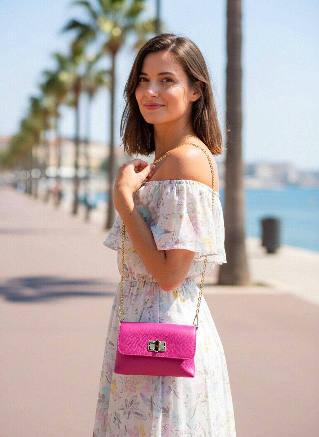 Modella con a floral off the shoulder dress carries a rosa leather shoulder bag con a gold chain strap.