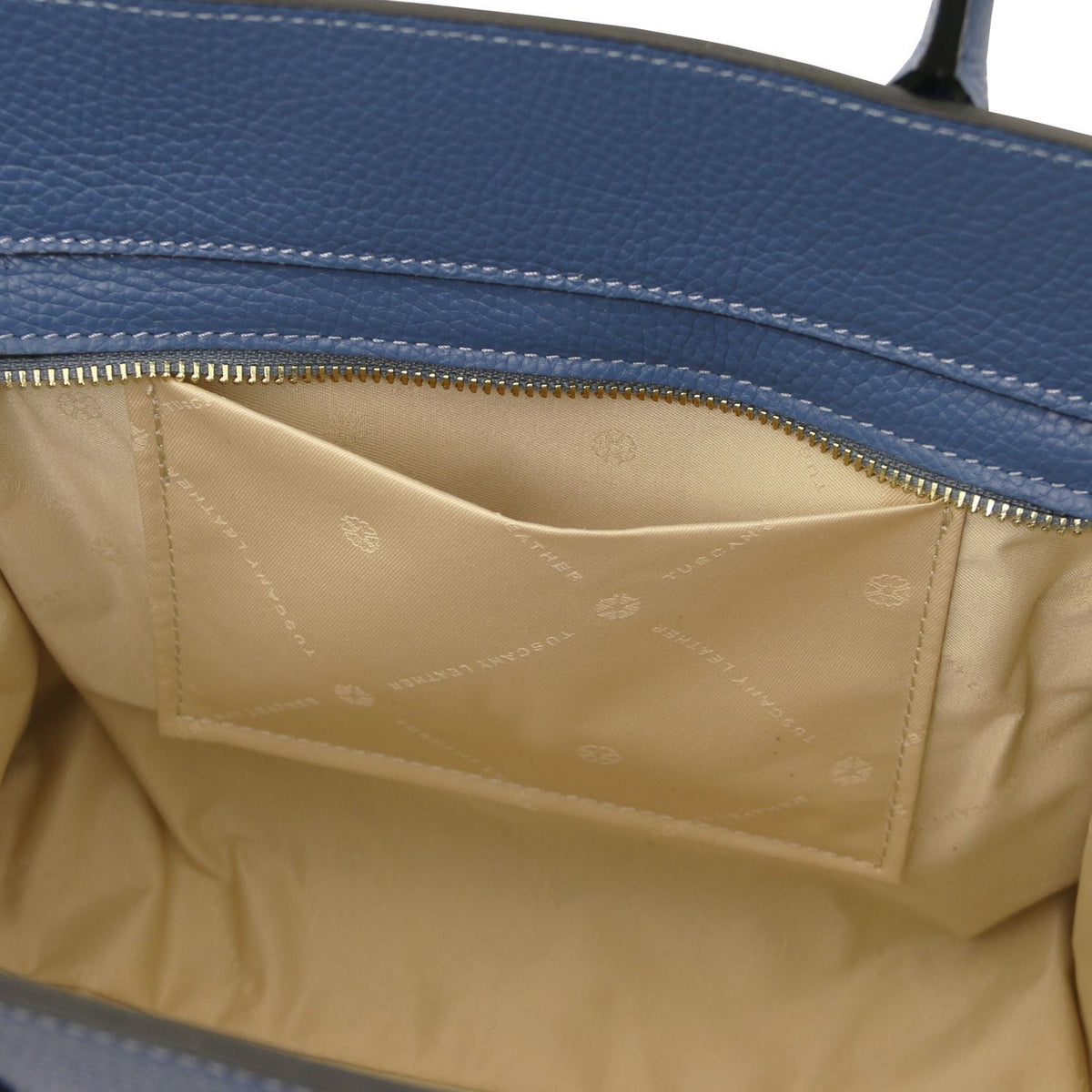 Abierto view of blue leather tote mostrando beige fabric interior pocket with subtle branding and detailed stitching inside zippered compartment.