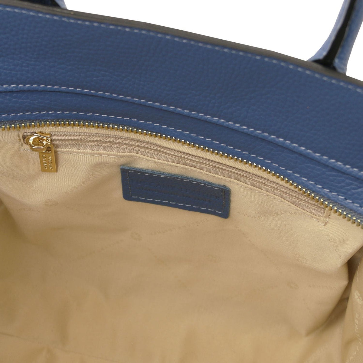 Vista interior of blue bolso tote de piel italiana mostrando beige forro de tela, interior bolsillo con cremallera with tirador dorado, and stitched leather label.