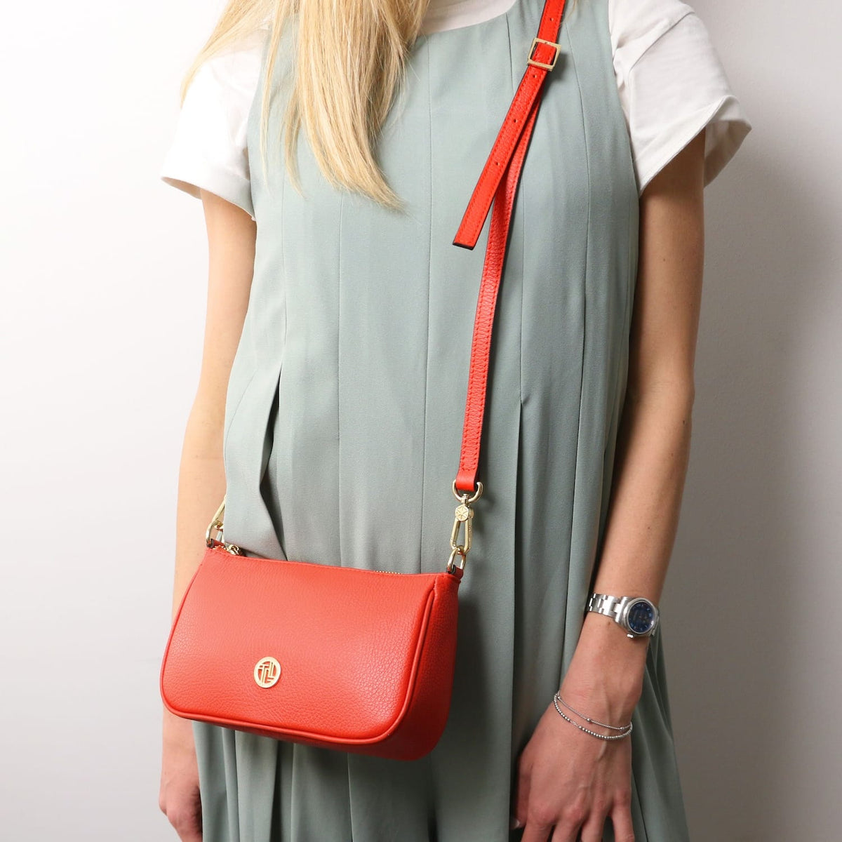 Parfait leather crossbody bag in bright coral with gold hardware and a long adjustable strap worn over the shoulder