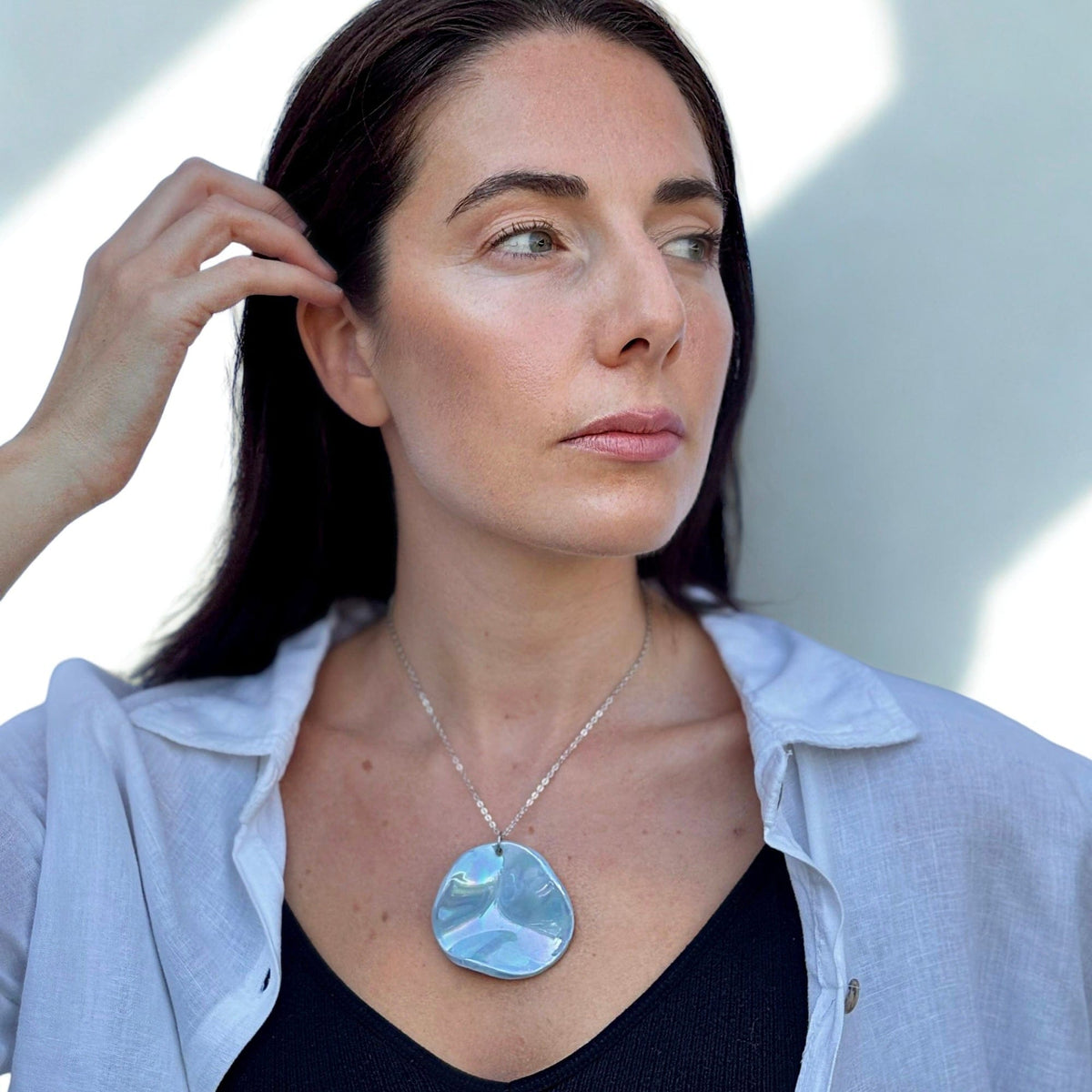 Woman wearing a light blue iridescent ceramic pendant necklace on a silver chain