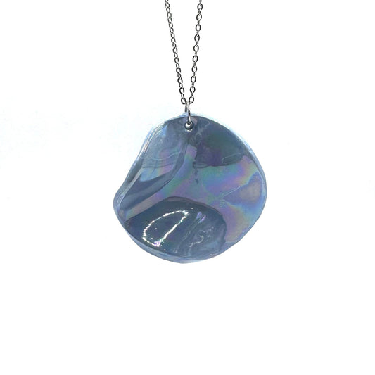 Iridescent blu ceramic pendant necklace on a silver chain against a bianco background