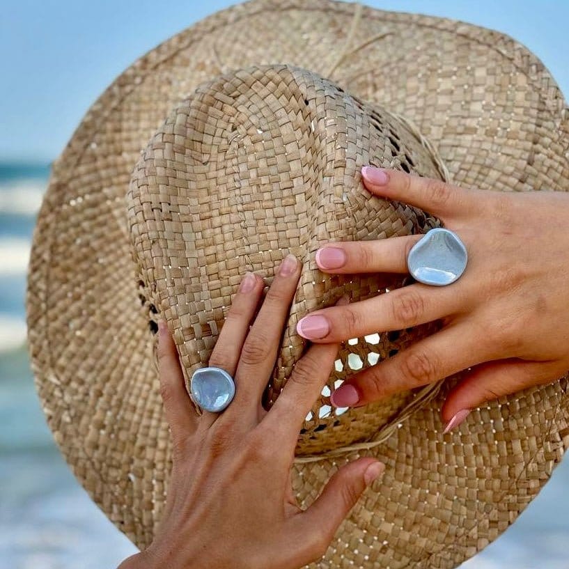 Two azzurro pearl ceramic Perla rings on fingers con a woven straw hat in the background.