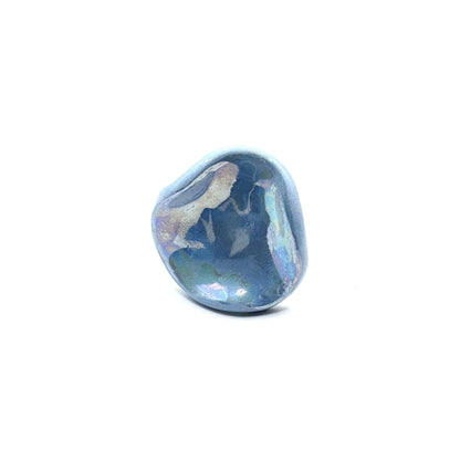 Primo piano of a single azzurro pearl ceramic ring con an irregular rounded shape on a bianco surface.