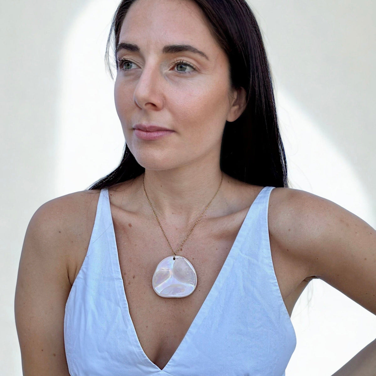 Mannequin porcognact pearl-pink ceramic pendant necklace on a gold chain over a bleu clair V-neck top