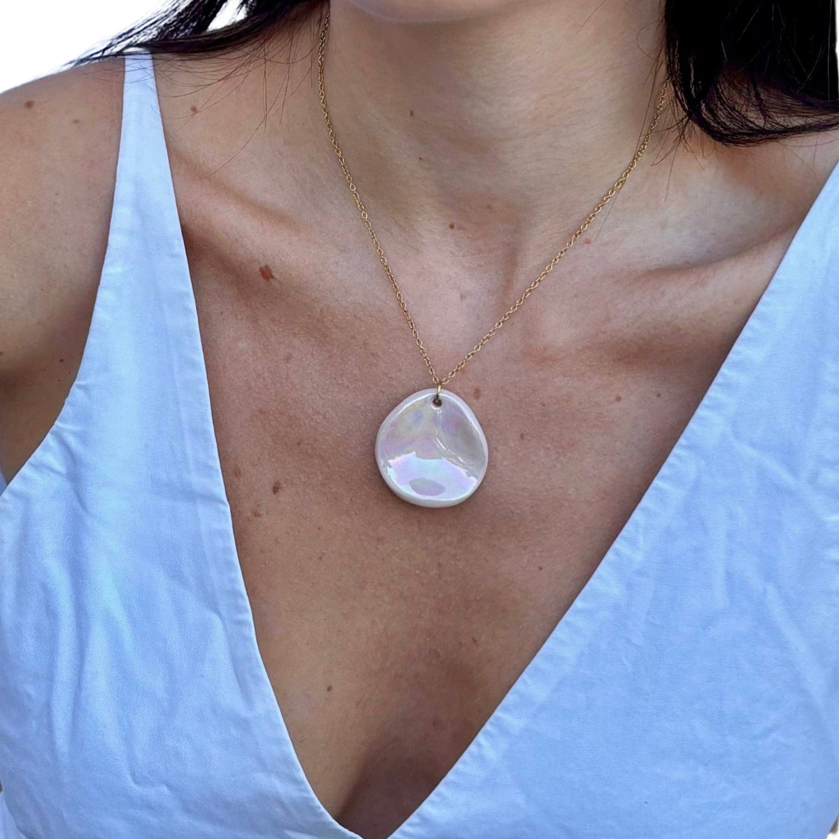 Handcrafted pearl pink ceramic pendant on a delicate gold chain worn on a bleu clair top