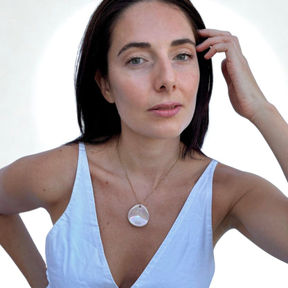 Portrait of a femme porcognact a handcrafted pearl pink ceramic necklace with a round iridescent pendant on a thin gold chain