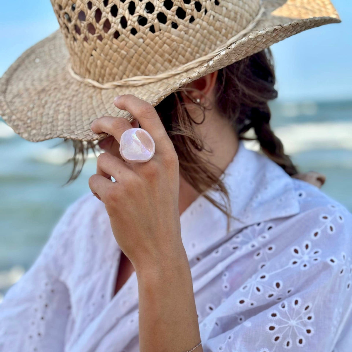 Pearl pink ceramic ring worn on a finger with a straw hat in the background