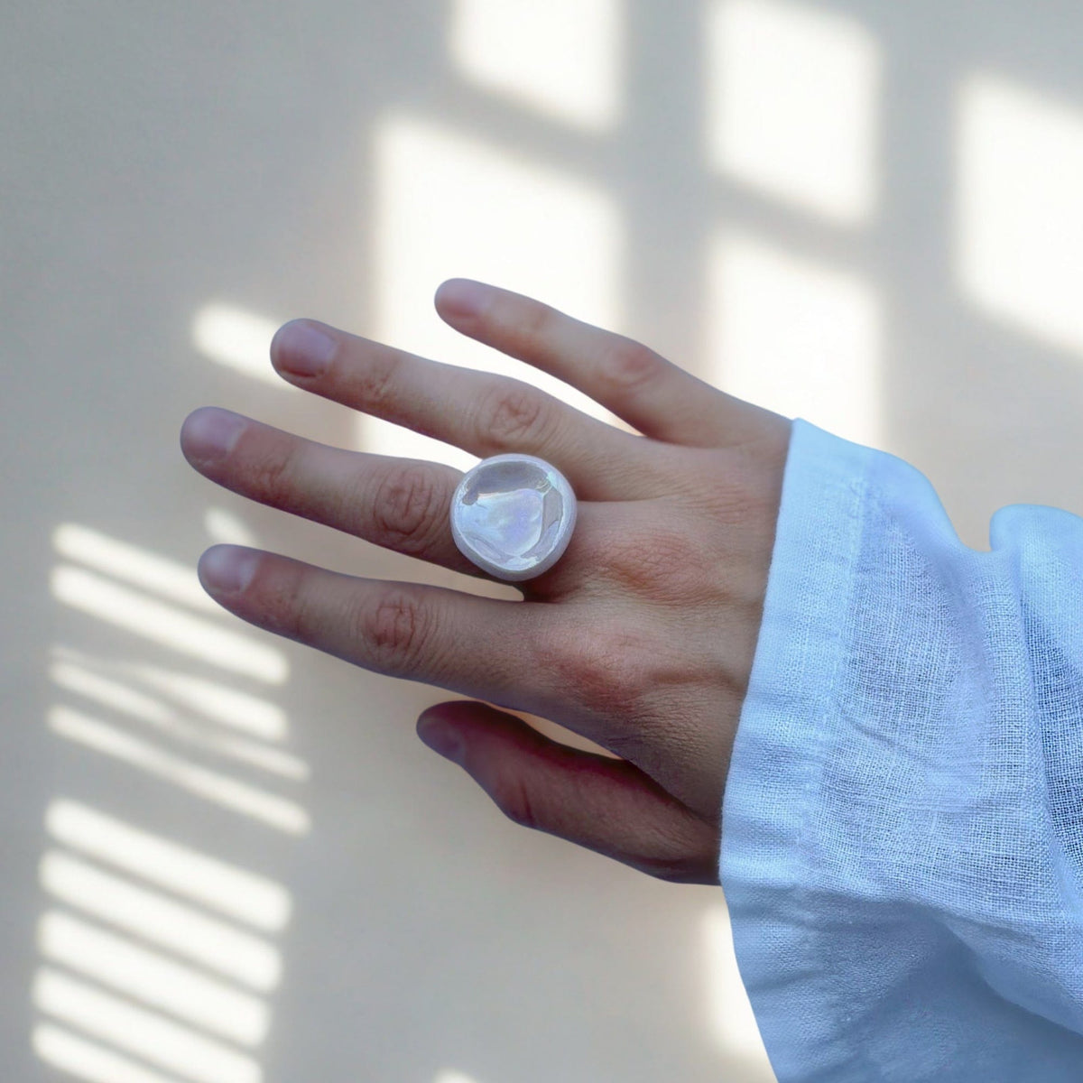Close up of a hand wearing a round pearl pink ceramic ring from the Perla collection