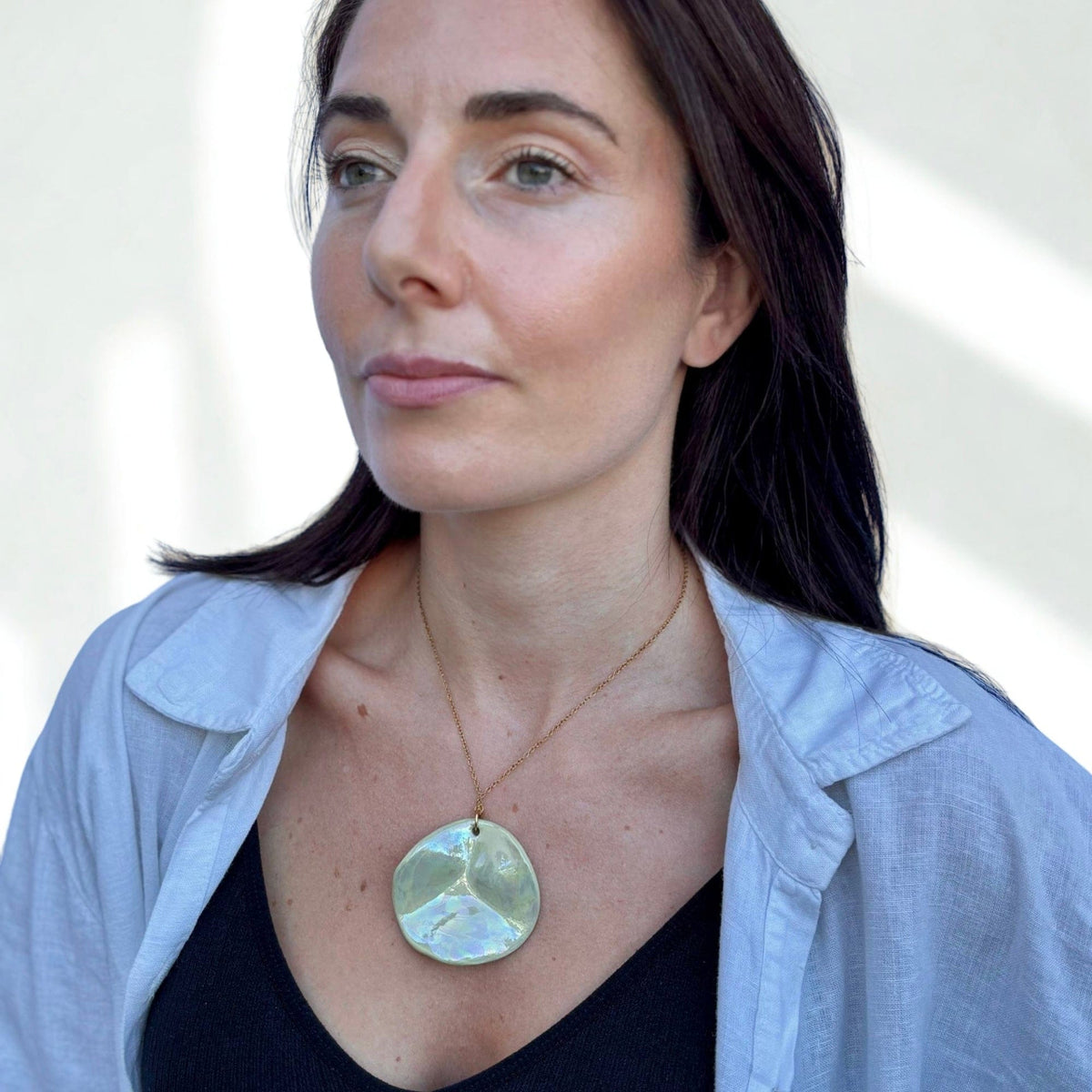 Mannequin porcognact a large round sage green ceramic pendant necklace on a delicate gold chain.