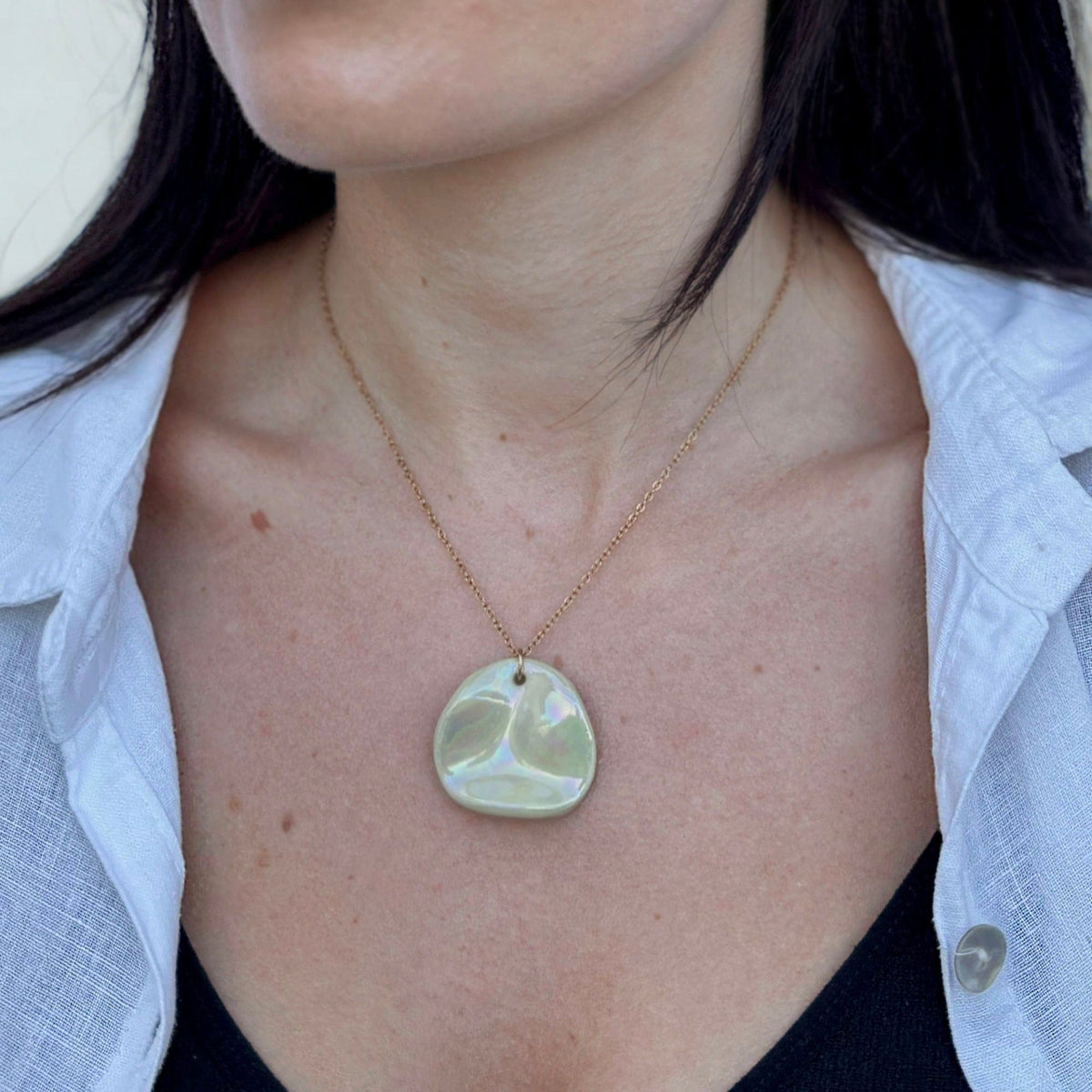 Gros plan of the Perla necklace pendant in sage-green ceramic on a delicate gold chain.