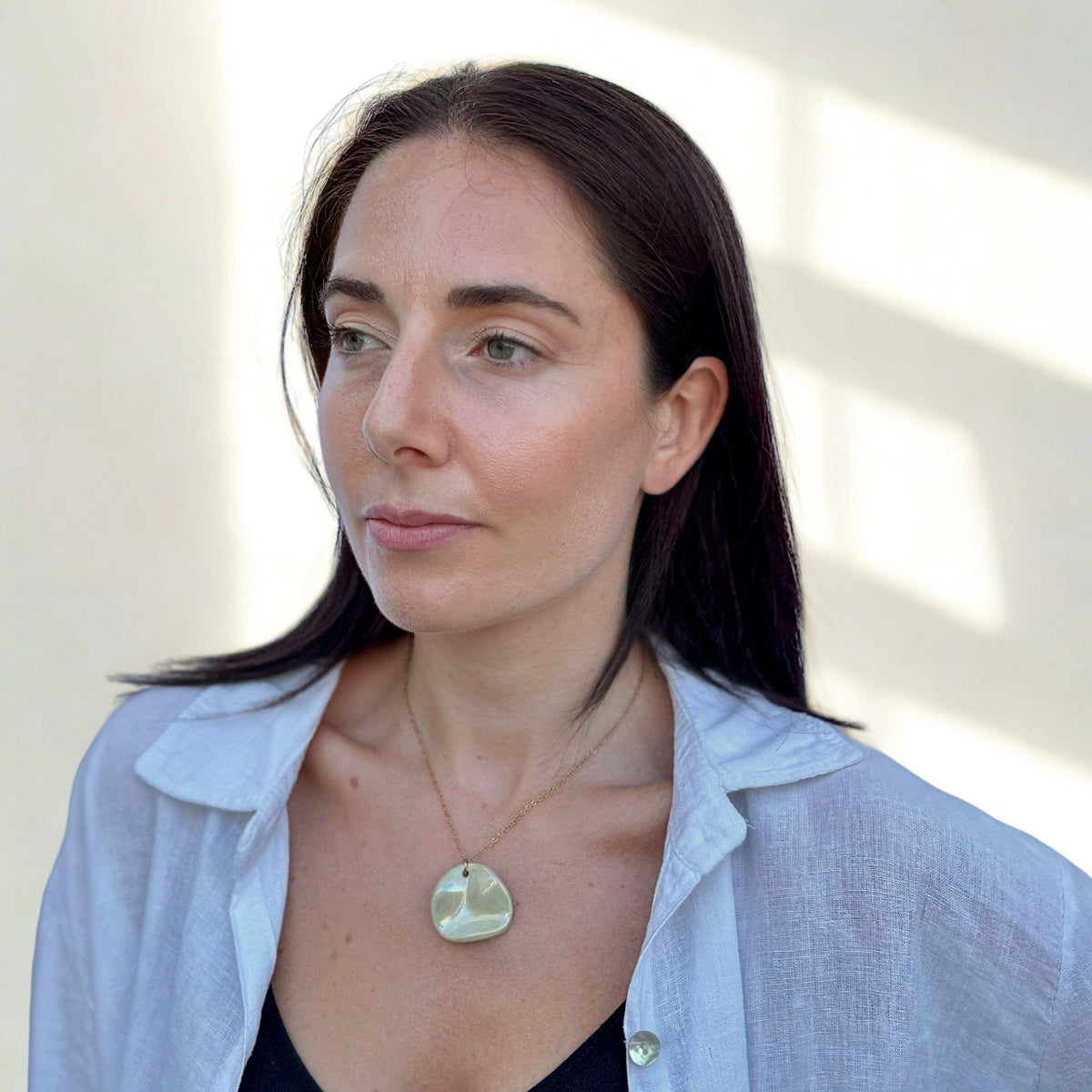 Portrait of a femme porcognact the Perla sage-green ceramic pendant necklace on a gold chain.