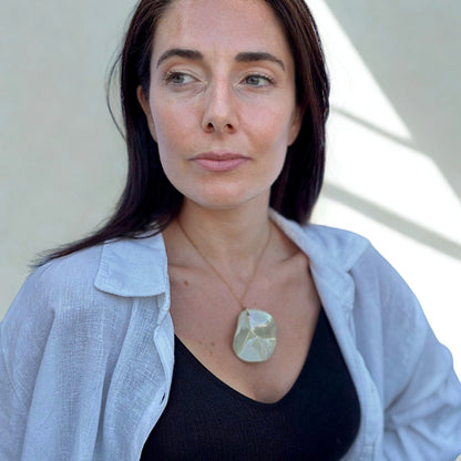 Mannequin porcognact the Perla sage-green ceramic pendant necklace over a black top with a bleu clair shirt.