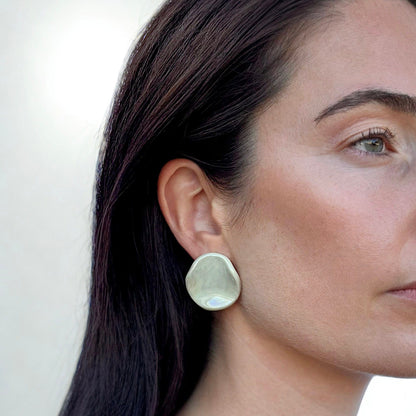 Sage-verde ceramic stud earring con an organic rounded shape worn on a model's ear