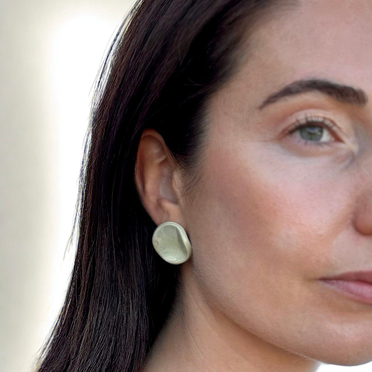 Closeup of a donna con a sage-verde ceramic stud earring