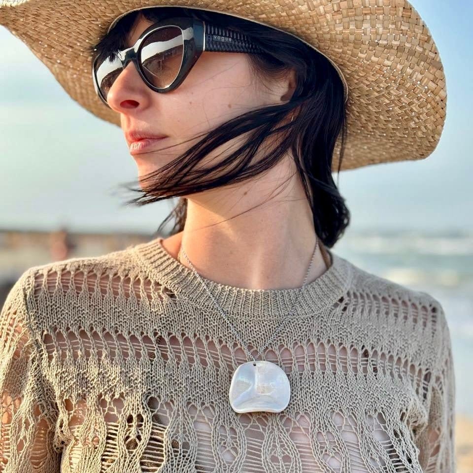 Mujer con a large handcrafted pearl-white cermic necklace with a straw hat and sunglasses with a blurred beach background