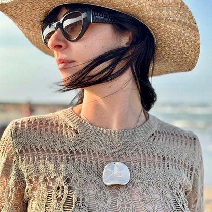 Mujer con a large handcrafted pearl-white cermic necklace with a straw hat and sunglasses with a blurred beach background